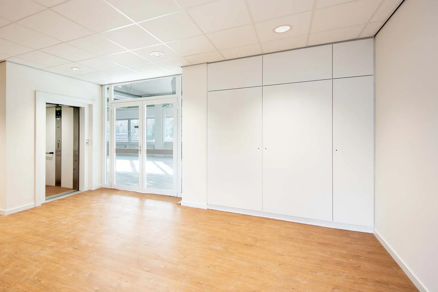 Lichte en moderne hal met lift, houten vloer en glazen deuren aan de Huis-ter-Heideweg.